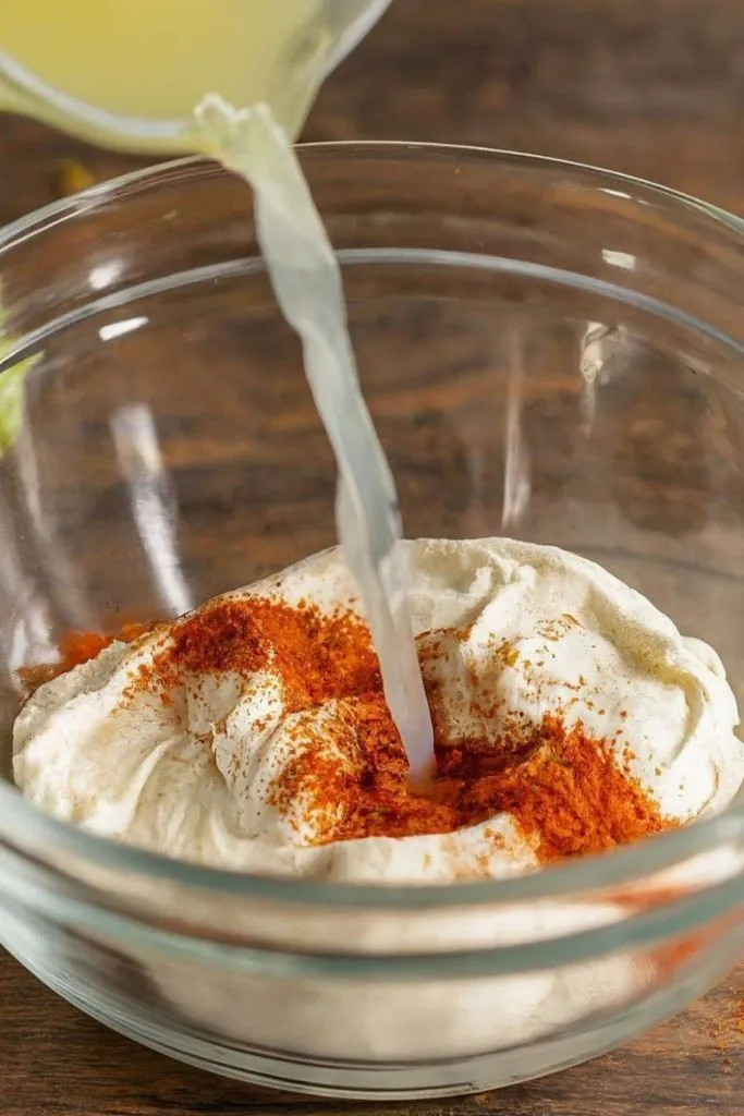 An image in which lime juice is being added in a bowl containing sour cream and taco seasoning.